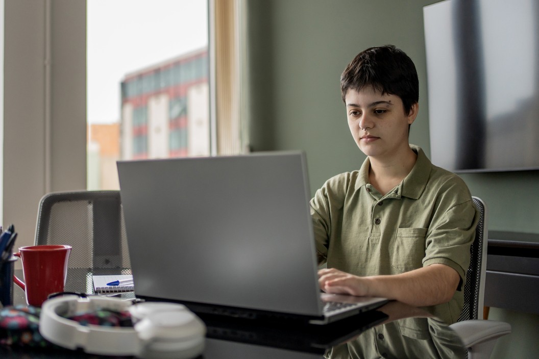 Person sat at a desk working on a laptop with headphones next to them.